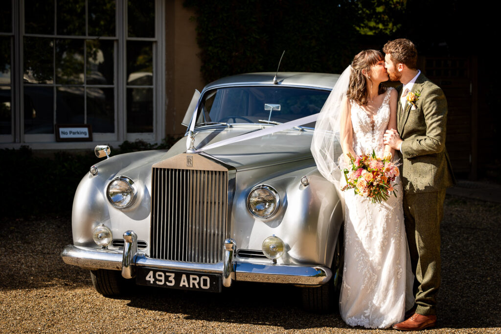 Newly married couple kissing by their wedding car.