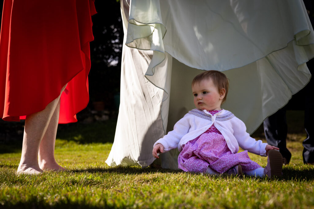 A baby shaded by a dress at a wedding reception.