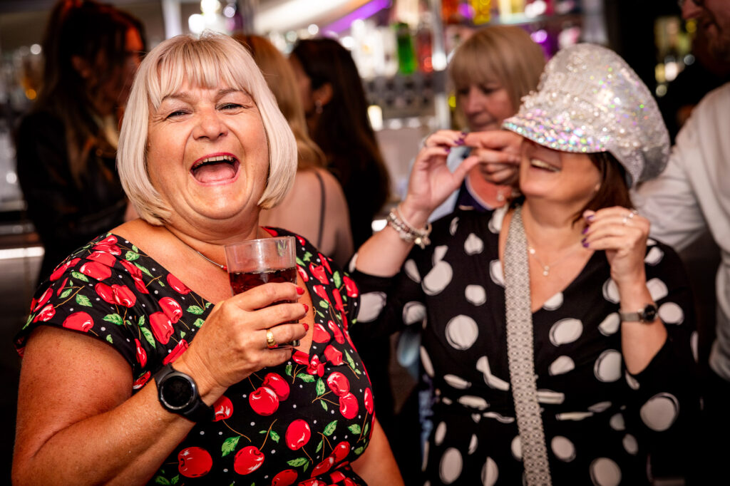 Laughing wedding guests wearing a hat.